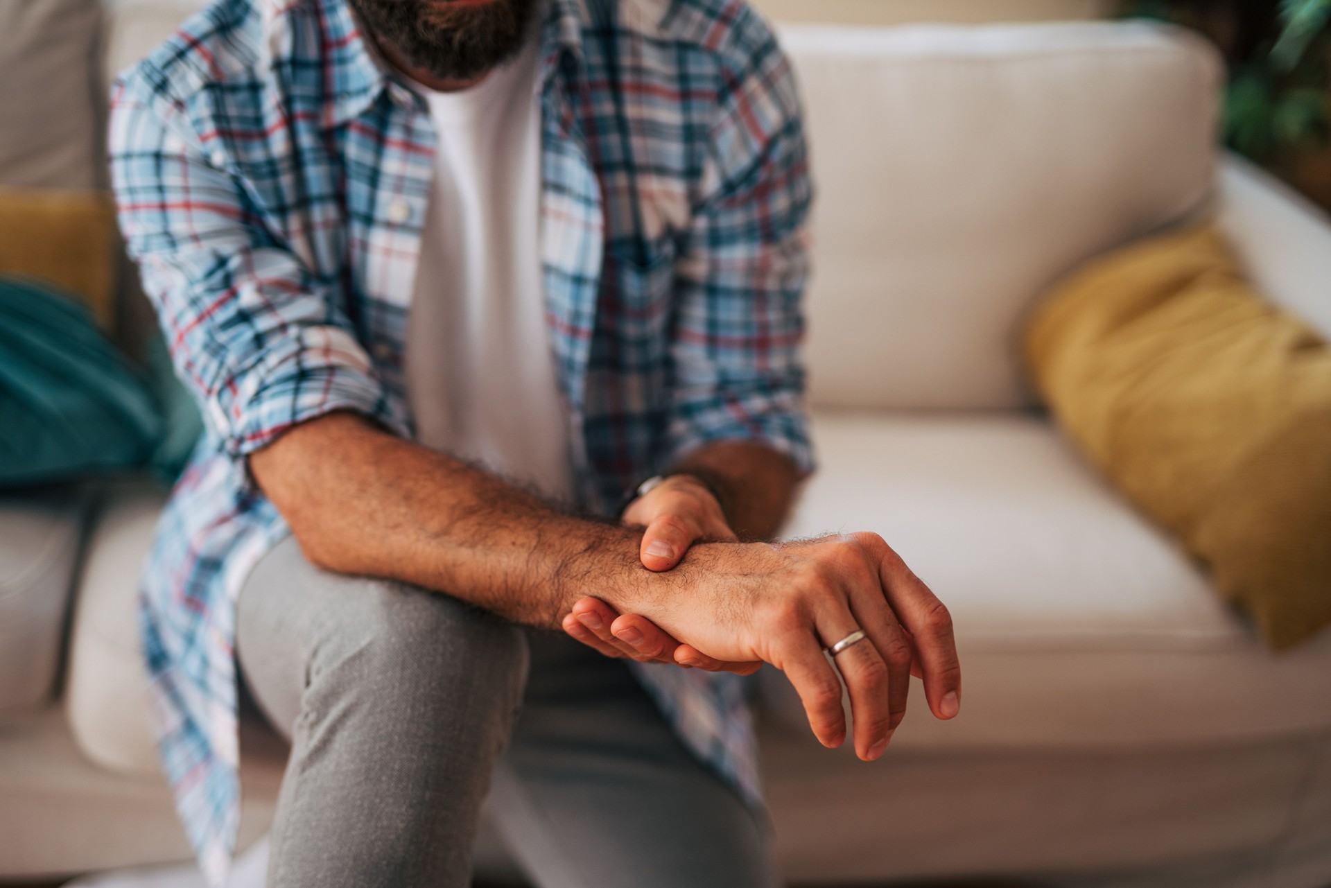 Man experiencing wrist pain while sitting on sofa at home Man experiencing wrist pain while sitting on sofa at home